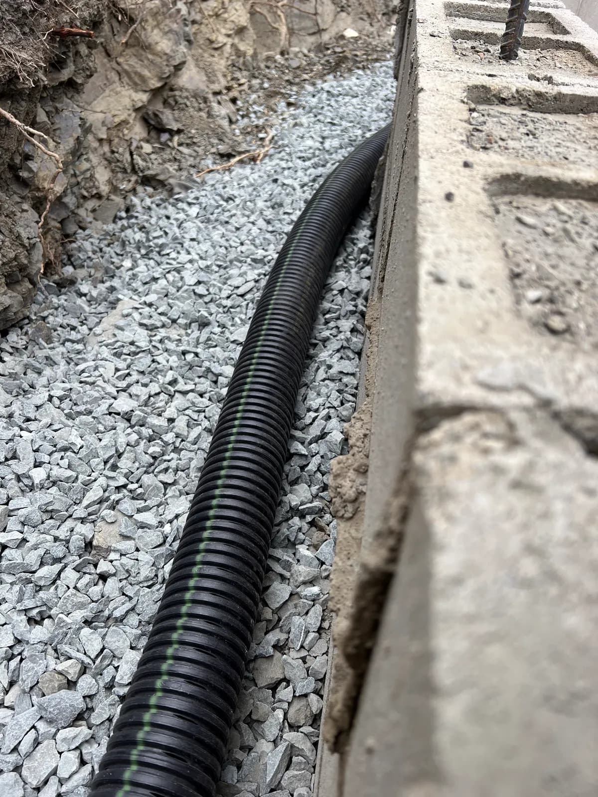 Perforated pipe bedded in drainage gravel behind a block wall