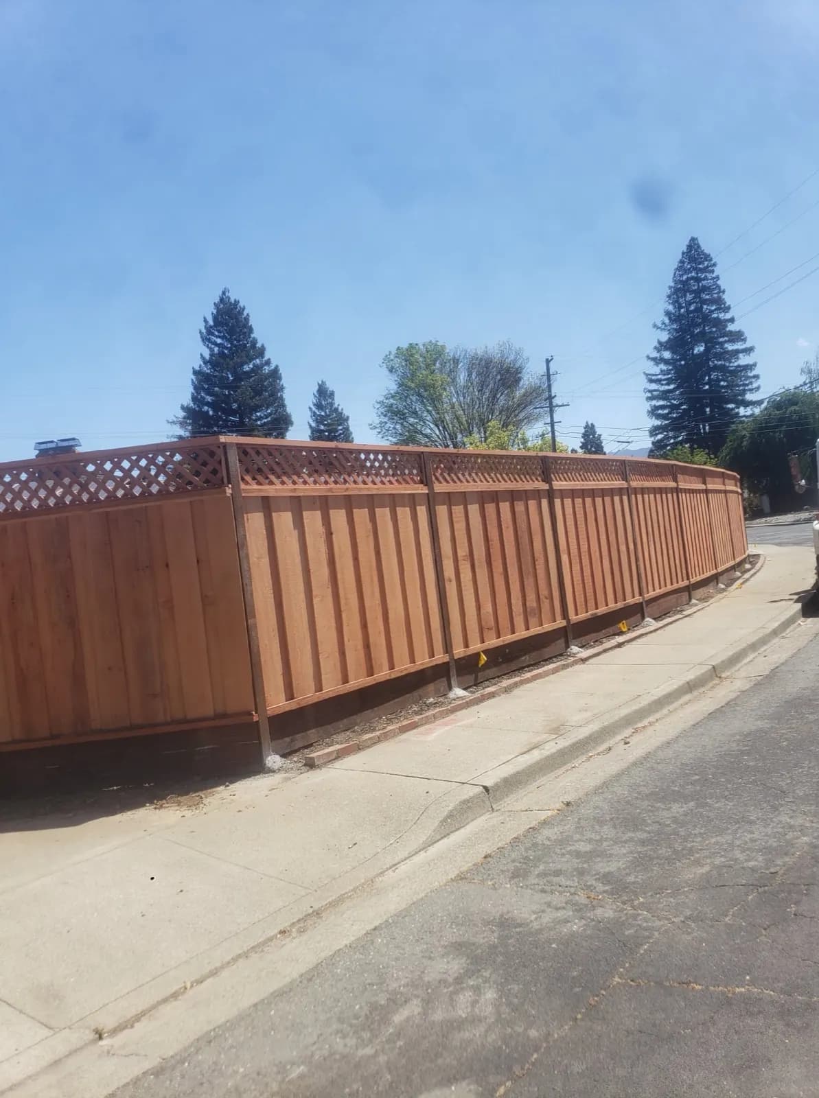 Finished redwood privacy fence with lattice top wrapping a corner lot